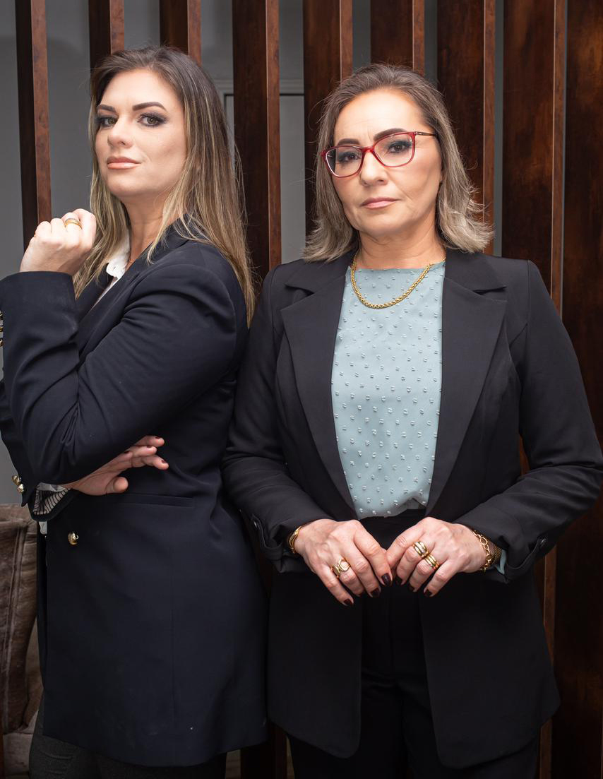 Advogadas Valle & Metzelthin em frente ao painel de madeira